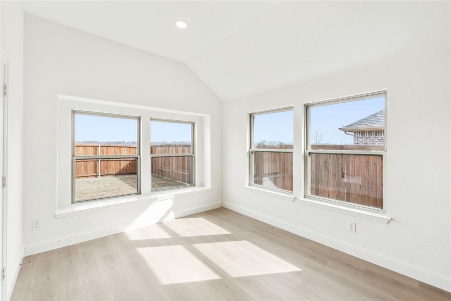 Empty room with vaulted ceiling, light wood floors, and five windows overlooking a fenced backyard Empty room with vaulted ceiling, light wood floors, and five windows overlooking a fenced backyard
