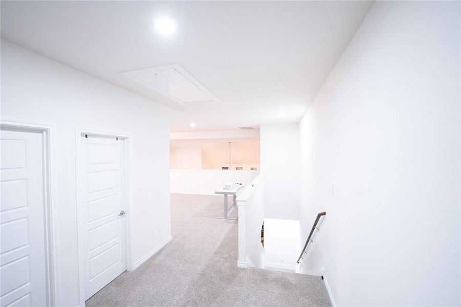 Upper-level landing featuring light gray carpet, recessed lighting, white panel doors, and a white stair railing with a dark wood-finish handrail Upper-level landing featuring light gray carpet, recessed lighting, white panel doors, and a white stair railing with a dark wood-finish handrail