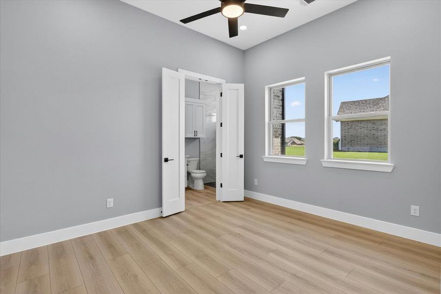 Spacious room featuring light wood-finish flooring, light gray walls, and two large double-hung windows