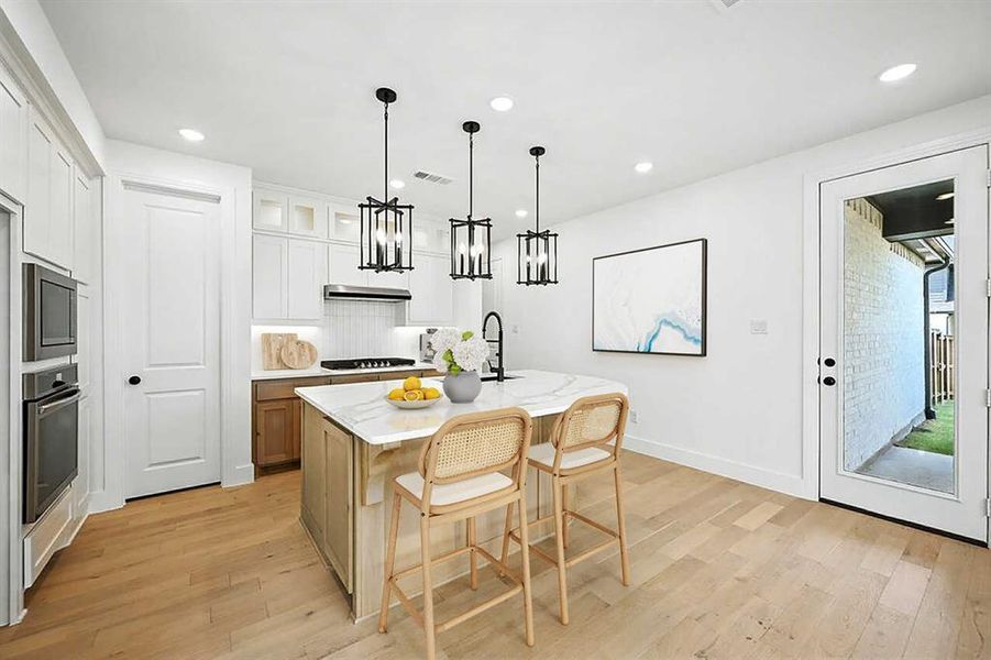 Kitchen with a breakfast bar, hanging light fixtures, light wood-type flooring, tasteful backsplash, and recessed lighting Kitchen with a breakfast bar, hanging light fixtures, light wood-type flooring, tasteful backsplash, and recessed lighting
