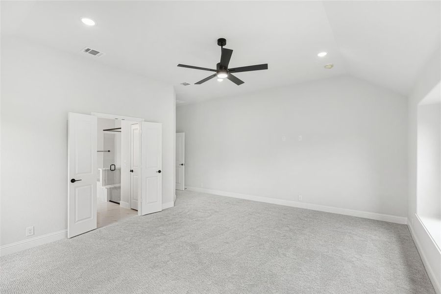 Empty bedroom with gray carpet, vaulted ceiling, black ceiling fan, and open walk-in closet doors Empty bedroom with gray carpet, vaulted ceiling, black ceiling fan, and open walk-in closet doors