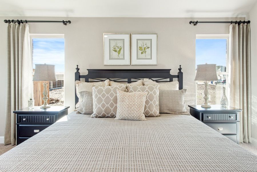 Bedroom with king bed, dark wood headboard, two nightstands, and windows with neutral drapes on each side Bedroom with king bed, dark wood headboard, two nightstands, and windows with neutral drapes on each side
