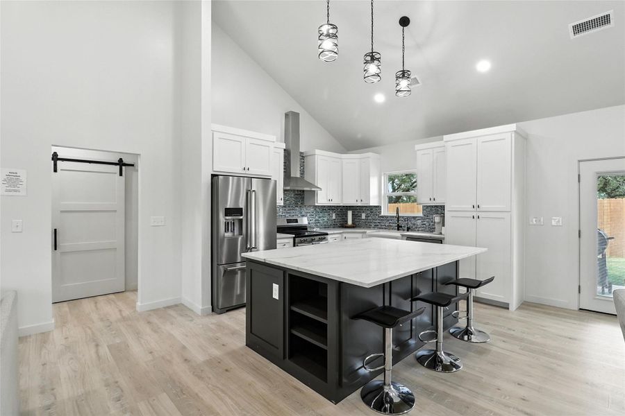Kitchen with a barn door, a breakfast bar, open shelves, stainless steel appliances, and white cabinetry