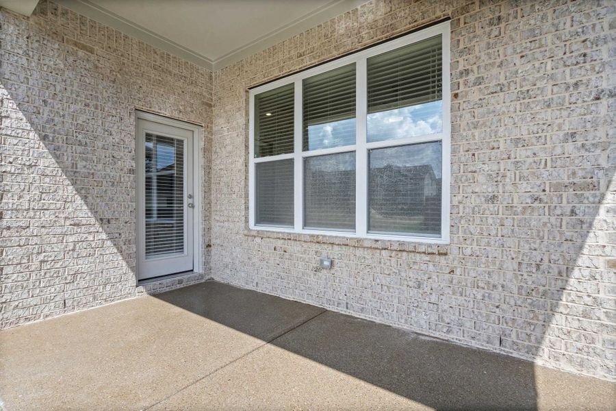 Covered patio with a light-colored brick exterior, a full-lite exterior door, and a large multi-pane window