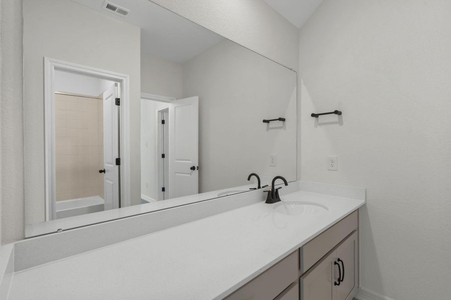 The secondary bath features tile flooring, custom stained cabinetry and light countertops and a shower/tub combo. Perfect for accommodating any visiting family and friends.
