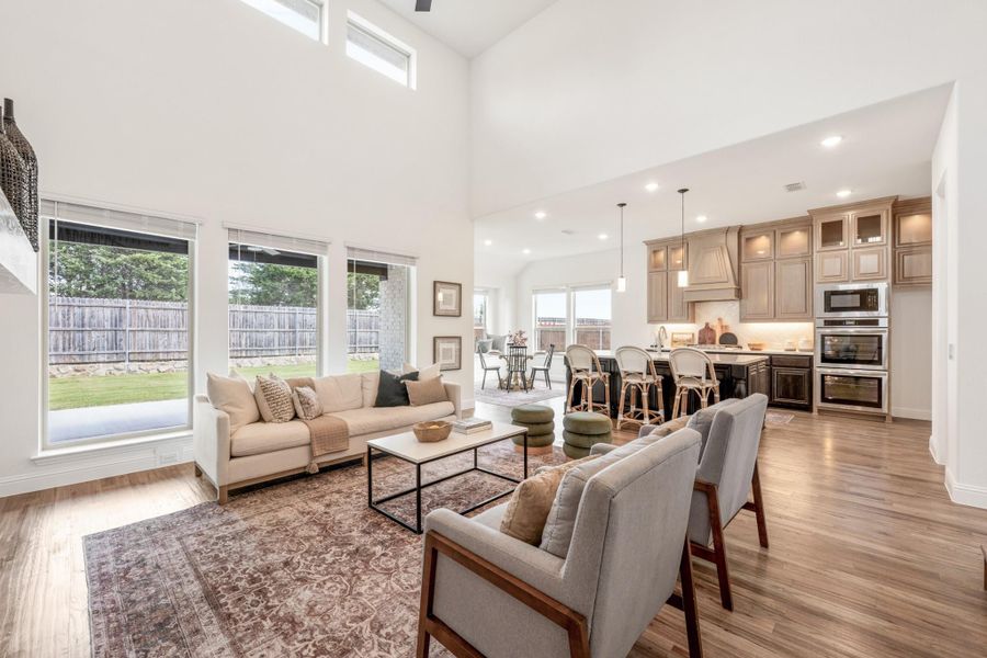 Open-concept living room with vaulted ceiling, hardwood floors, and kitchen visible in background
