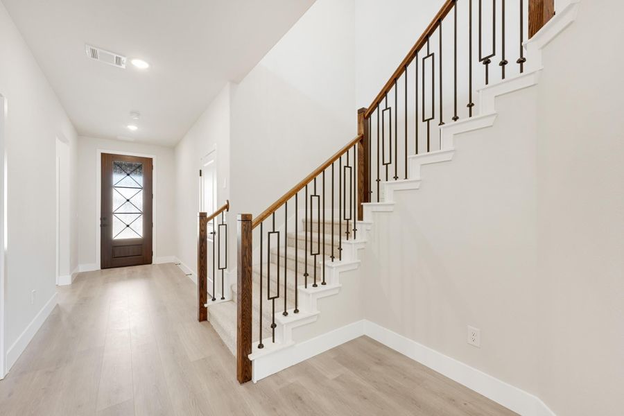 Entryway with staircase featuring wood handrail, iron balusters, and light hardwood floors leading to a front door.