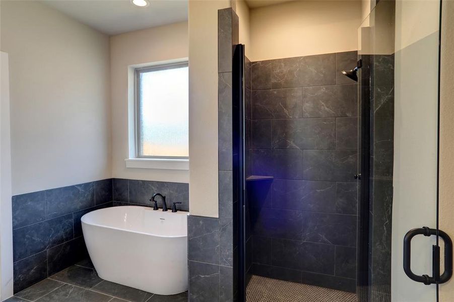 Bathroom featuring tile walls, a shower stall, a freestanding bath, tile patterned flooring, and a wainscoted wall Bathroom featuring tile walls, a shower stall, a freestanding bath, tile patterned flooring, and a wainscoted wall