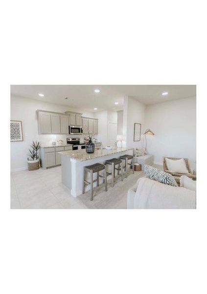 Kitchen featuring appliances with stainless steel finishes, a kitchen bar, gray cabinets, a kitchen island with sink, and light stone counters