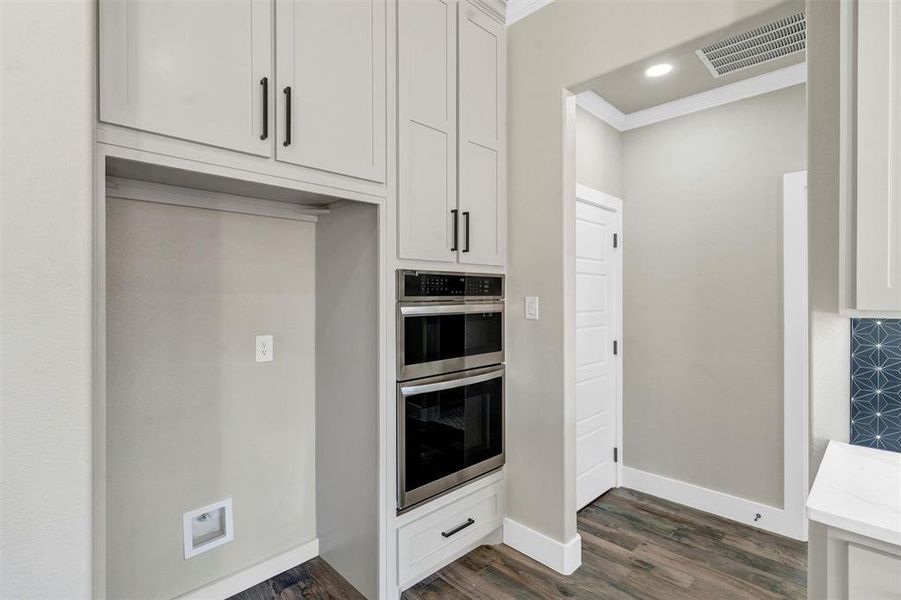 Kitchen featuring white cabinetry, double oven, dark hardwood / wood-style flooring, and ornamental molding