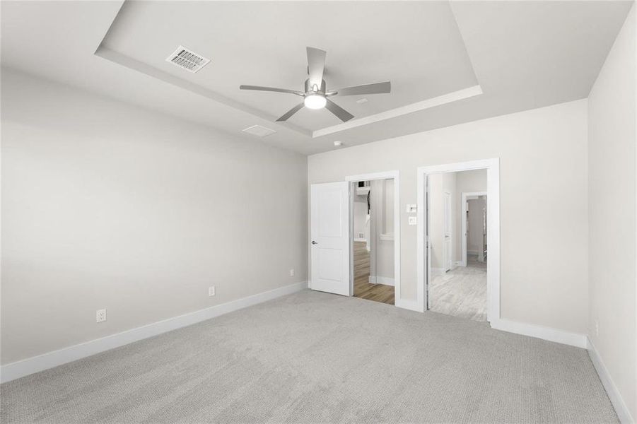 Spacious room with light gray carpeting, tray ceiling, and a modern ceiling fan with integrated lighting Spacious room with light gray carpeting, tray ceiling, and a modern ceiling fan with integrated lighting