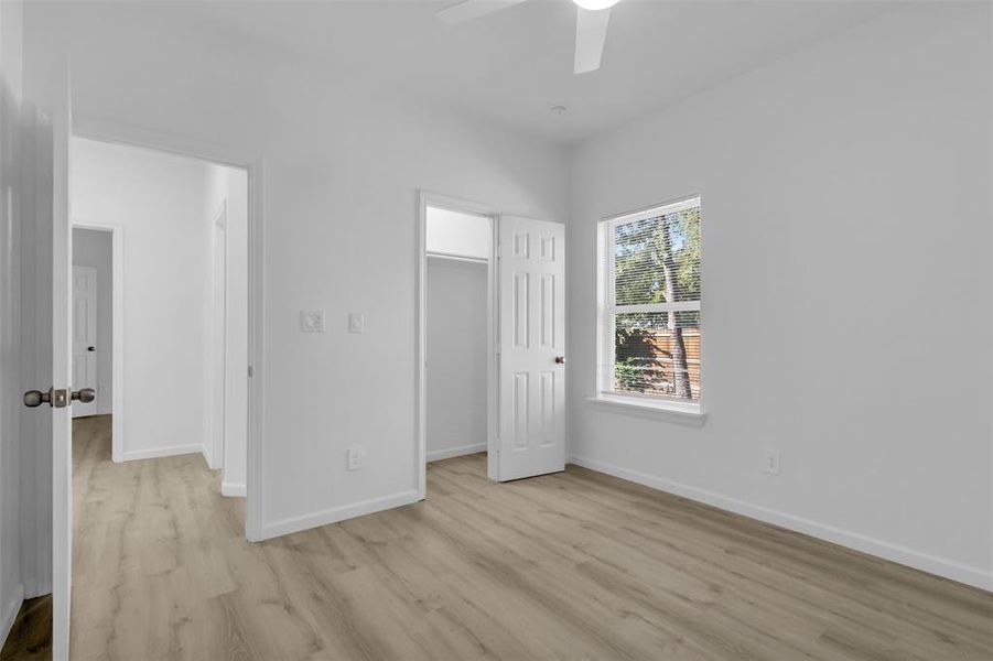 Unfurnished bedroom with a spacious closet, light wood-style flooring, and a ceiling fan