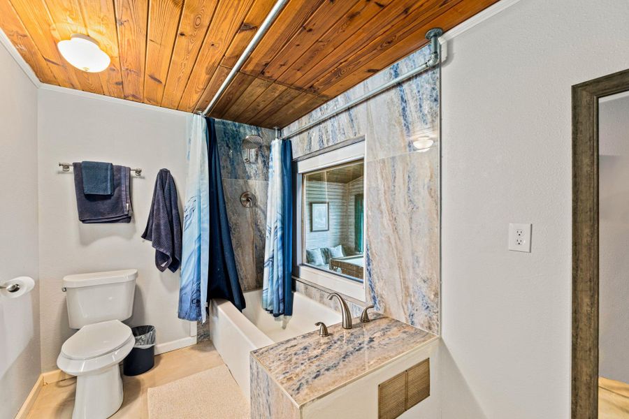 Bathroom featuring a wood-panel ceiling, full-height tile shower surround, and a built-in vanity with a stone countertop