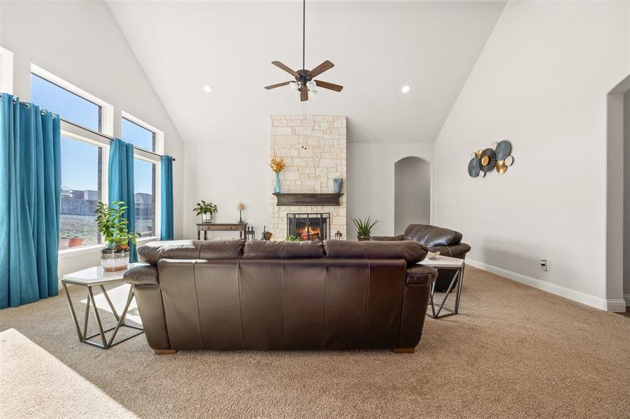 Living room with ceiling fan, high vaulted ceiling, carpet floors, and a stone fireplace Living room with ceiling fan, high vaulted ceiling, carpet floors, and a stone fireplace