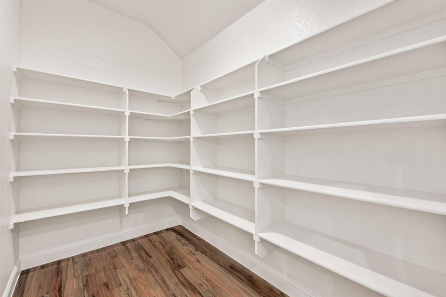 Walk-in pantry with white built-in shelves on three walls and hardwood floors