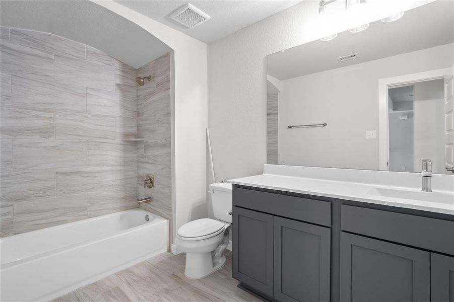 Secondary bathroom features light countertops and grey cabinets, neutral paint, shower/tub combo with tile surround, large mirror, tile floors, sleek fixtures and modern finishes, plenty of space to accommodate any visiting family or guests.