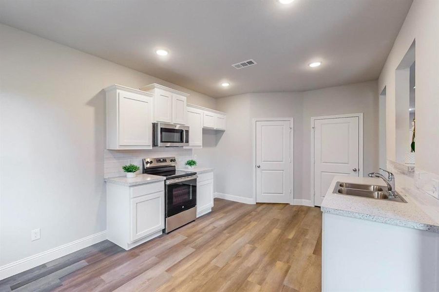 Kitchen with tasteful backsplash, appliances with stainless steel finishes, white cabinetry, light wood-type flooring, and sink