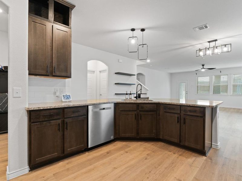 Kitchen with sink, hanging light fixtures, light wood-type flooring, dishwasher, and light stone countertops