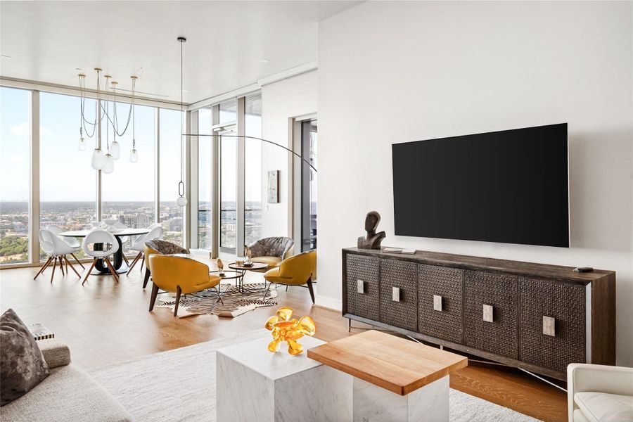 This is a modern, high-rise apartment featuring an open-plan living area with a sleek kitchen, a comfortable lounge space, and a dining area, all bathed in natural light from floor-to-ceiling windows that offer expansive city views.