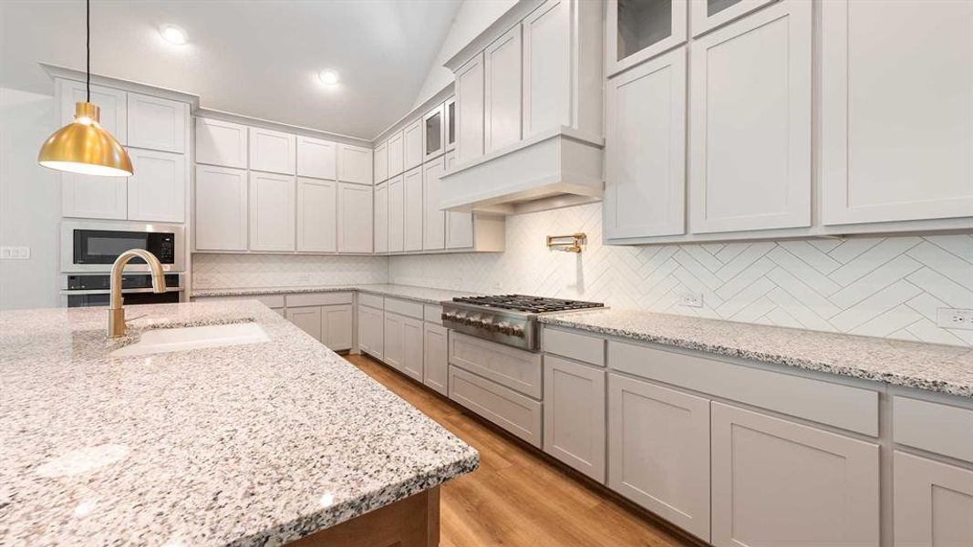 Kitchen featuring tasteful backsplash, stainless steel appliances, sink, light stone counters, and light hardwood / wood-style flooring