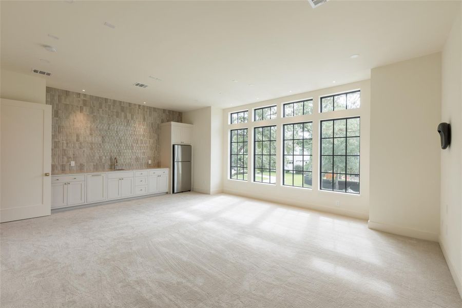 Bathed in natural light, the media room features a full wall of oversized grid windows and a stunning built-in wet bar with textured tile backsplash. Whether used for entertaining or relaxing, this space delivers both function and sophistication. Bathed in natural light, the media room features a full wall of oversized grid windows and a stunning built-in wet bar with textured tile backsplash. Whether used for entertaining or relaxing, this space delivers both function and sophistication.