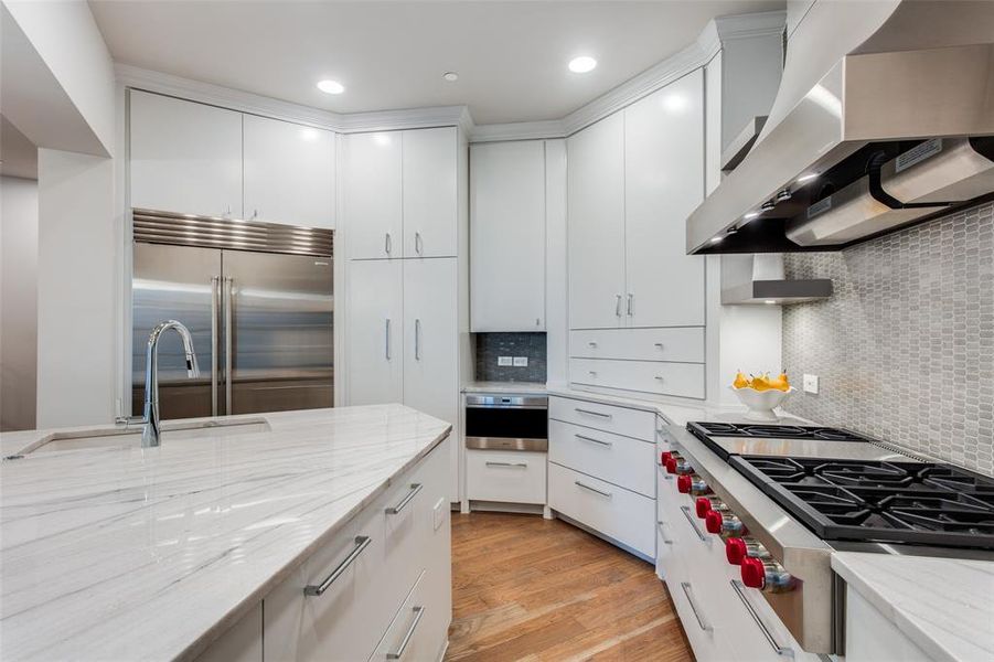 Kitchen with premium appliances, tasteful backsplash, wall chimney exhaust hood, sink, and light hardwood / wood-style flooring