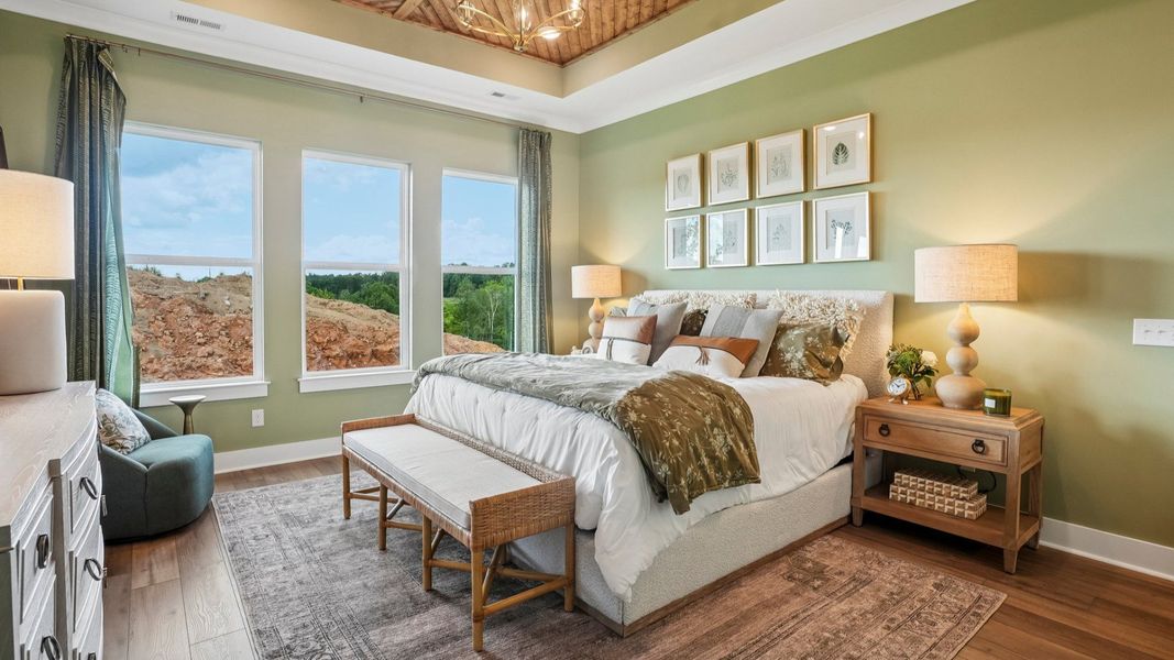 Primary suite with tray ceiling, windows, and hard surface flooring Primary suite with tray ceiling, windows, and hard surface flooring