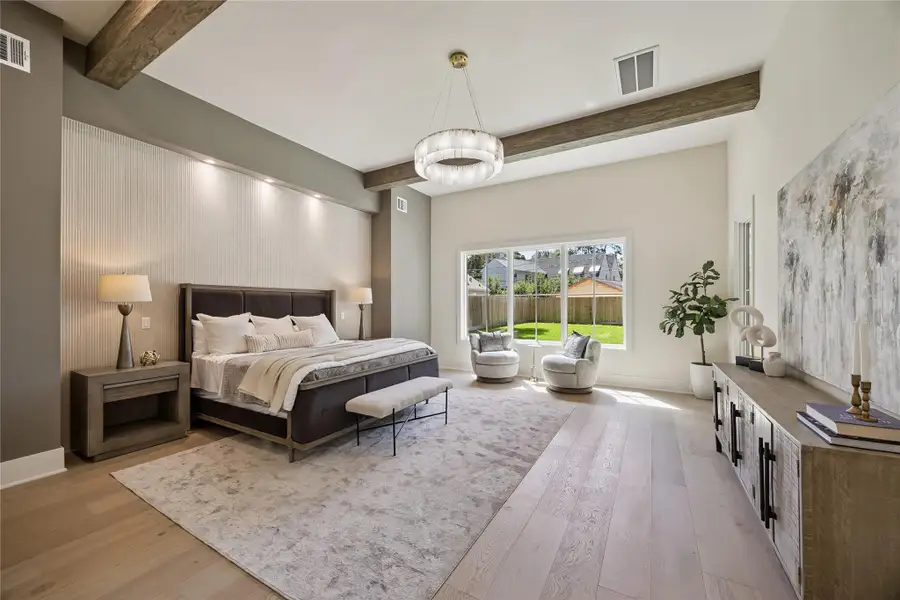 PRIMARY BEDROOM: Luxurious primary retreat featuring soaring ceilings with exposed wood beams, wide-plank hardwood floors, and serene backyard views through oversized windows.