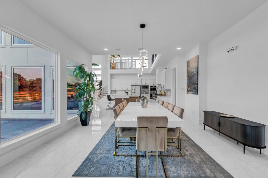 Dining Pavilion:Framed by walls of glass and anchored by designer lighting, the dining pavilion offers an atmosphere of modern refinement. The sleek table, flanked by plush seating with golden accents, sets the stage for intimate dinners or grand gatherings. With views into the kitchen and great room, every meal feels seamlessly connected to the heart of the home while bathed in natural light.