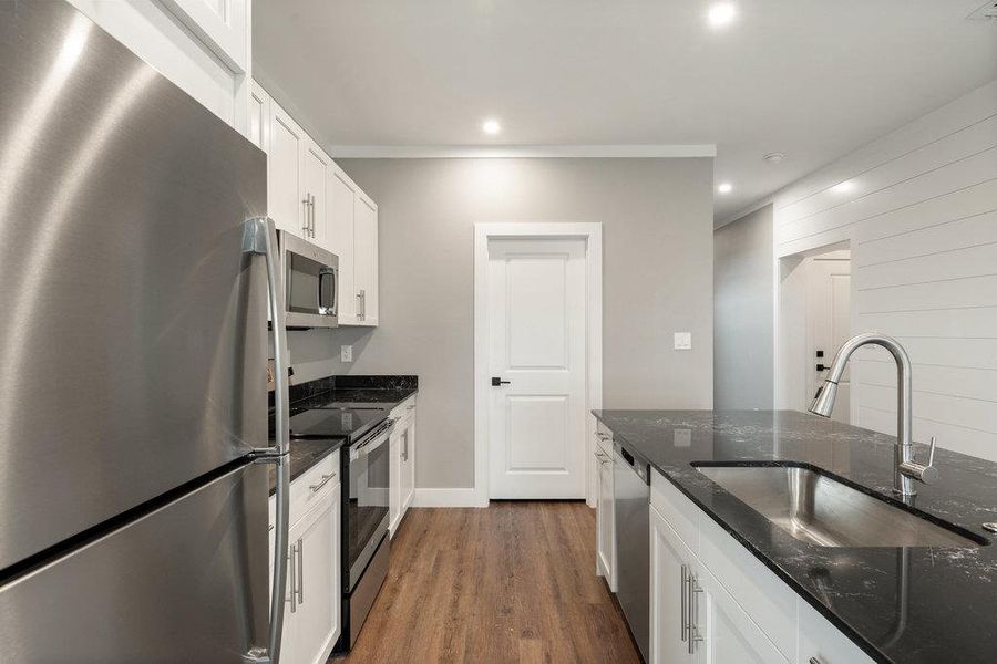 Kitchen featuring stainless steel appliances, dark quartz counters, white cabinets, dark wood-type flooring, and recessed lighting