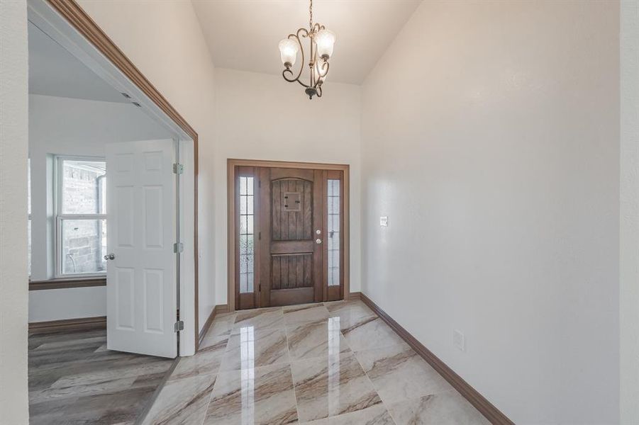 Entryway featuring a notable chandelier, marble finish floor, a high ceiling, and baseboards