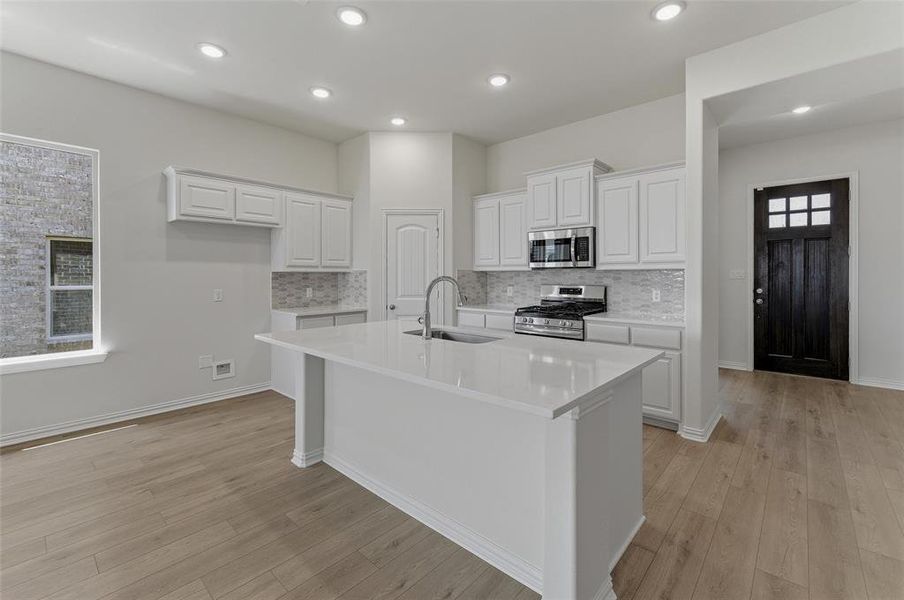 Bright kitchen featuring a central island with an undermount sink, white shaker cabinetry, stainless steel appliances, a tile backsplash, and recessed lighting Bright kitchen featuring a central island with an undermount sink, white shaker cabinetry, stainless steel appliances, a tile backsplash, and recessed lighting