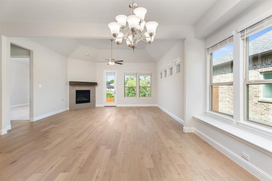 Unfurnished living room with a chandelier, light wood-type flooring, a tiled fireplace, a ceiling fan, and vaulted ceiling