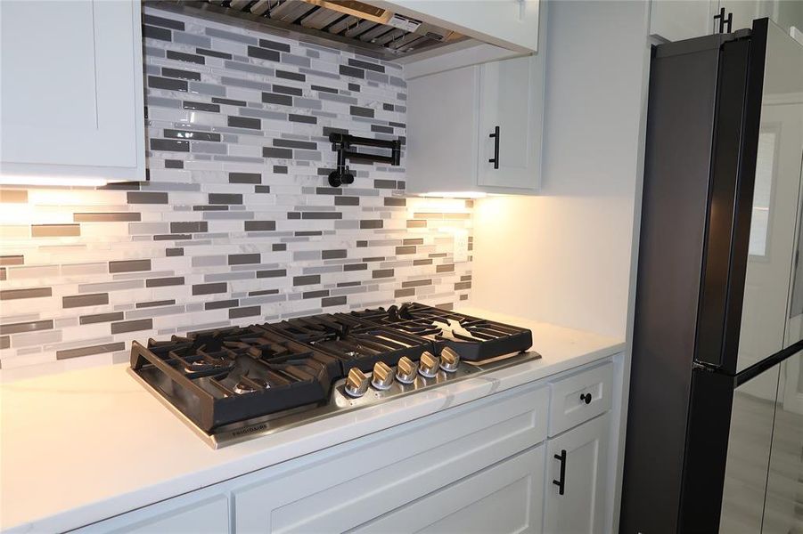 Kitchen with white cabinets, tasteful backsplash, stainless steel gas stovetop, freestanding refrigerator, and extractor fan