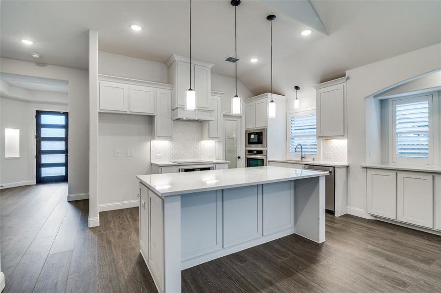 Kitchen featuring white cabinetry, sink, stainless steel appliances, lofted ceiling, and a kitchen island with lots of storage