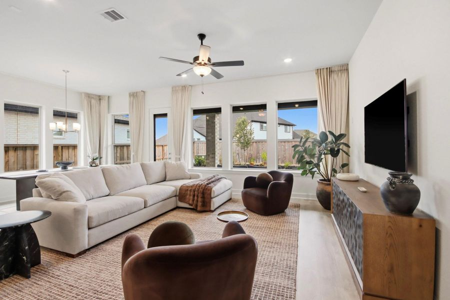 Bright living area featuring a cozy sectional sofa, modern armchairs, and large windows that flood the room with natural light, complemented by elegant decor and a wall-mounted TV.