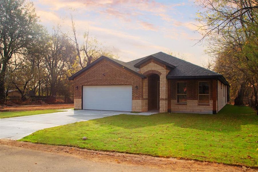 View of front of property with brick siding, driveway, an attached garage, a yard, and a shingled roof
