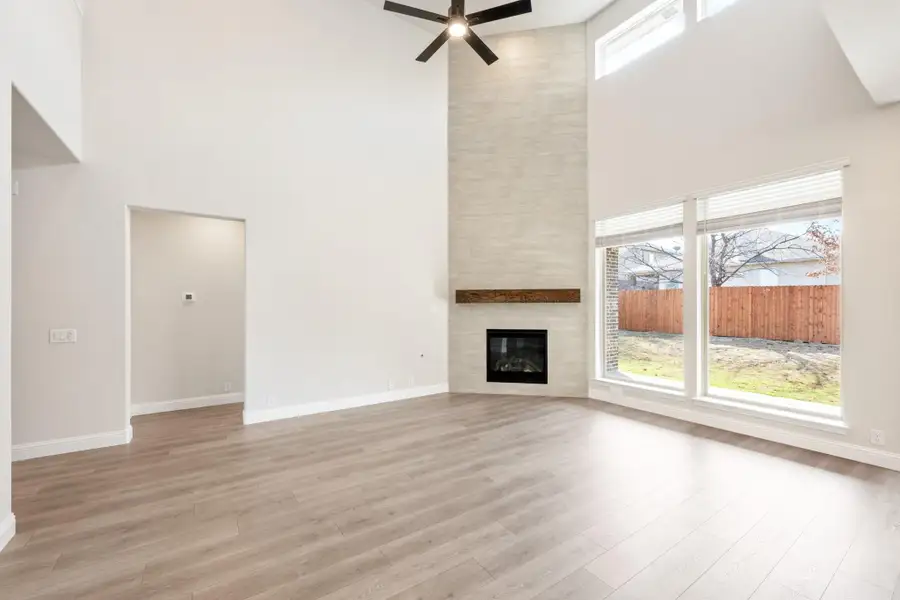 Open living room with high ceilings, tile fireplace, ceiling fan, and large windows with hardwood floors Open living room with high ceilings, tile fireplace, ceiling fan, and large windows with hardwood floors