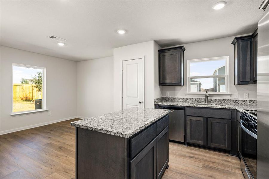 Kitchen with a center island, light stone countertops, light wood-type flooring, and recessed lighting Kitchen with a center island, light stone countertops, light wood-type flooring, and recessed lighting
