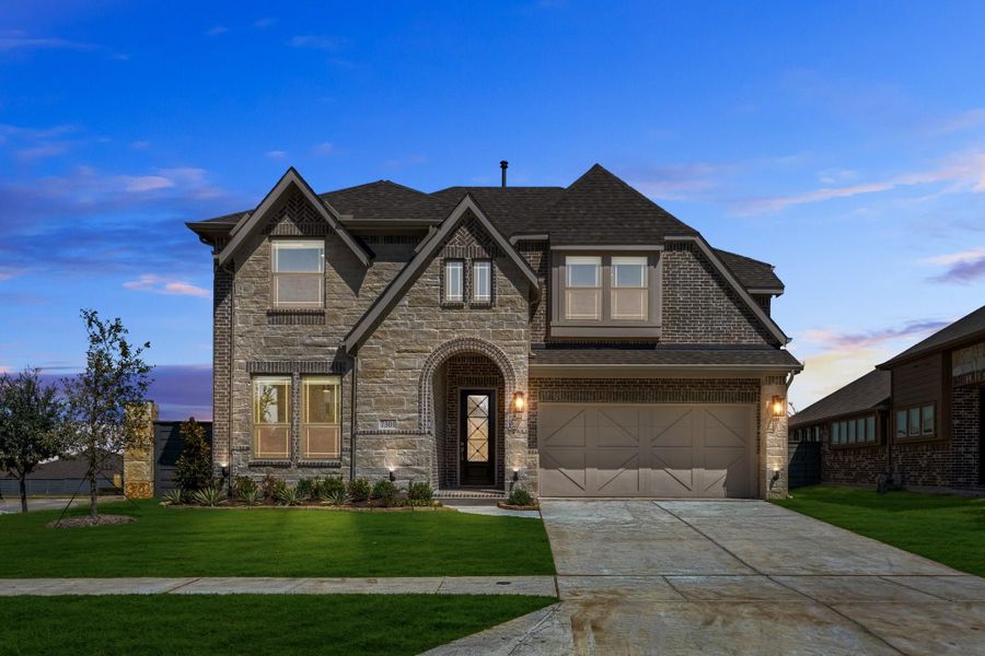 Two-story home with brick and stone exterior, arched entry, two-car garage, and green front lawn at dusk Two-story home with brick and stone exterior, arched entry, two-car garage, and green front lawn at dusk