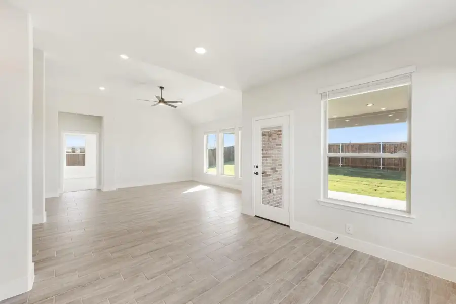 Open living area with vaulted ceiling, ceiling fan, wood-look tile floors, and back door with yard view