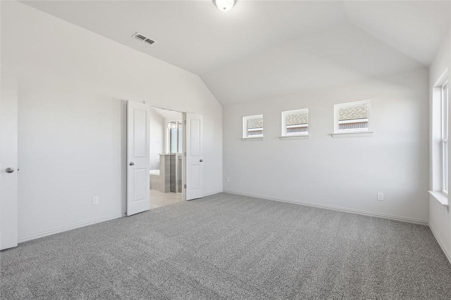 Unfurnished bedroom featuring lofted ceiling, light carpet, and ensuite bath