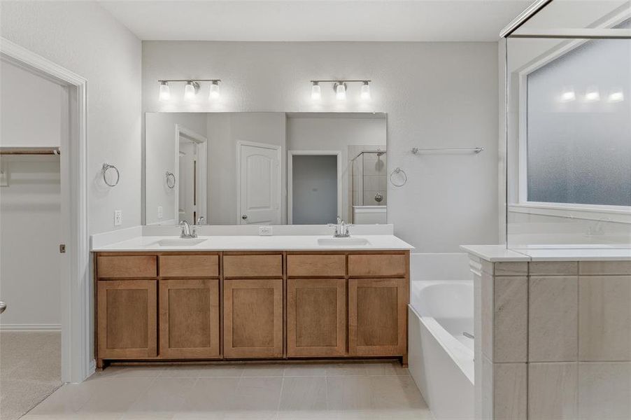 Spacious bathroom featuring a dual vanity with light wood-finish cabinetry and a white countertop, complemented by a large mirror and overhead lighting