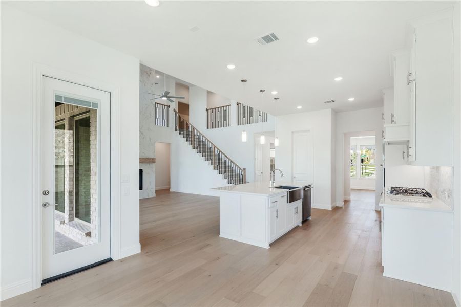 Open-concept kitchen with white island, light wood floors, and staircase visible in two-story living area