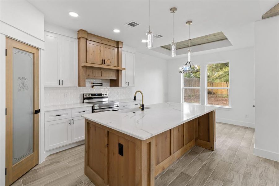 Kitchen featuring an island with sink, sink, stainless steel electric stove, and white cabinetry