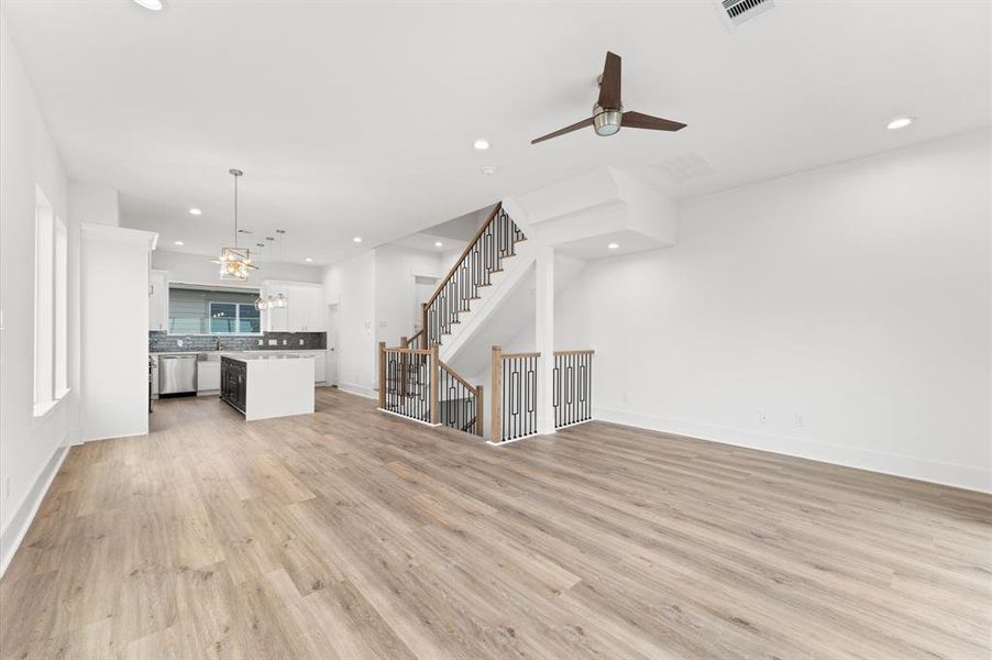 This modern open-concept living space features light wood flooring, a sleek kitchen with an island and stainless steel appliances, and an elegant staircase with metal railings. Perfect for entertaining and everyday living.