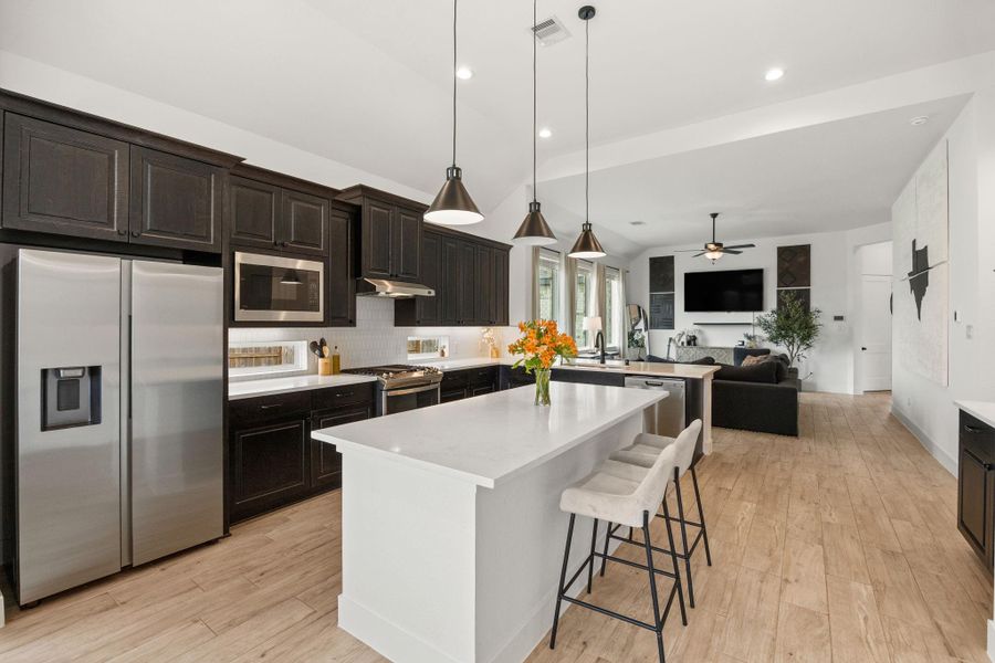Equipped with a gas range, built-in microwave, stainless refrigerator, and hex-pattern backsplash, this kitchen blends style with everyday functionality.