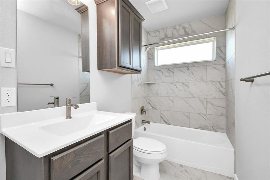 Secondary bath features tile flooring, bath/shower combo with tile surround, dark stainedwood cabinets, beautiful light countertop. Sample photo of completed home with similar floor plan. Actual colors and selections may vary.