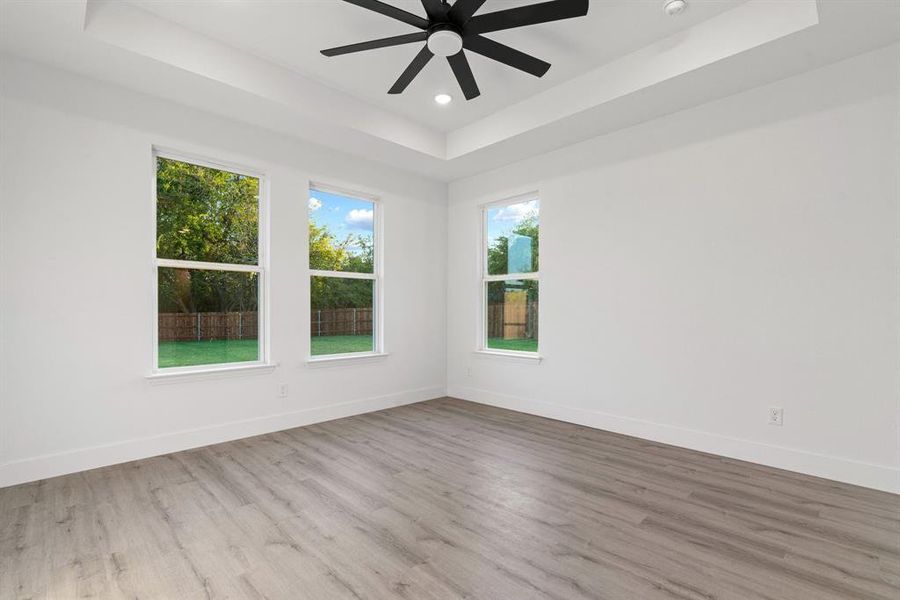 Empty room with ceiling fan, a tray ceiling, and light hardwood / wood-style flooring