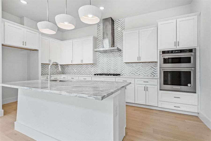 Kitchen with decorative backsplash, white cabinets, wall chimney range hood, light wood-type flooring, and sink